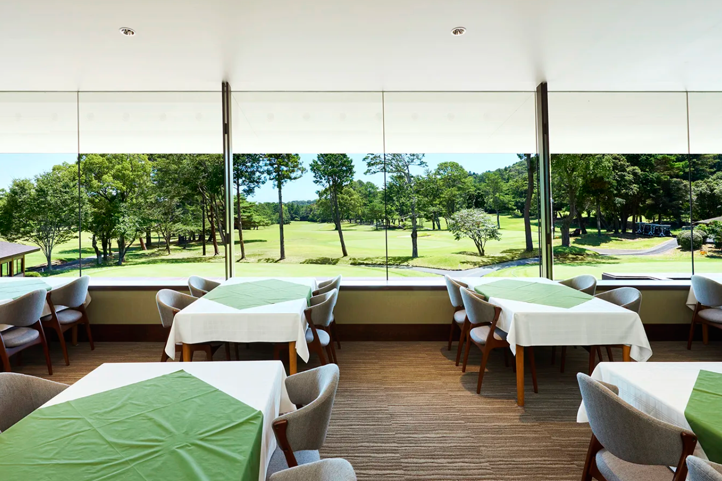 Dining area with tables and chairs near large windows overlooking a golf course.