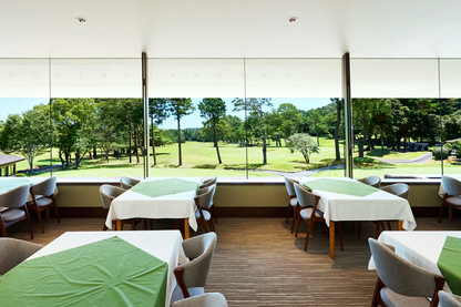 Dining area with tables and chairs near large windows overlooking a golf course.